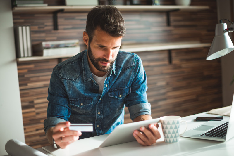 Man Holding a Credit Card whilst Staring at a Tablet | Paying Credit Agreements